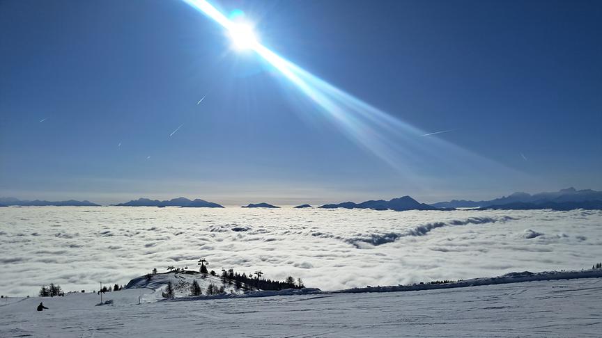 Blick auf die strahlende Sonne und das nebelverhangene Tal von der Skipiste aus