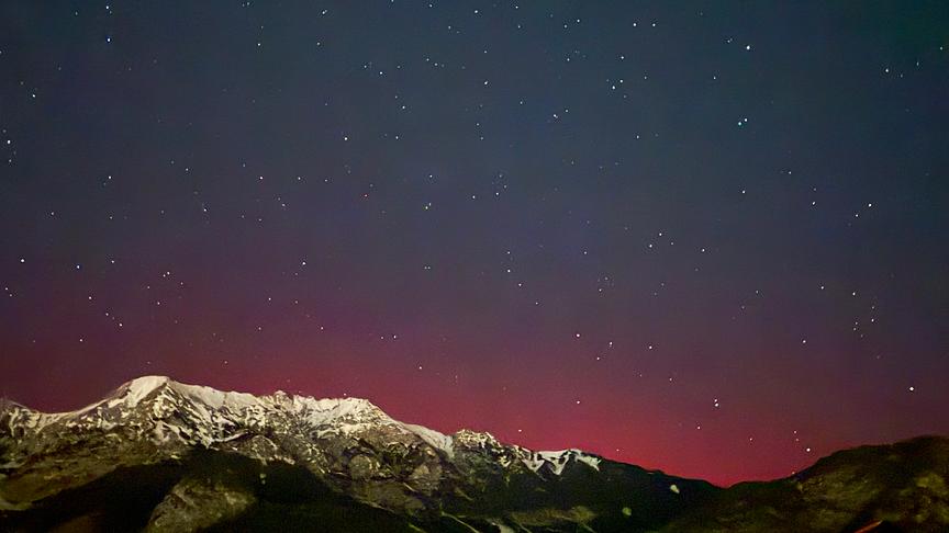 Rötliche Nordlichter hinter einer Bergkette