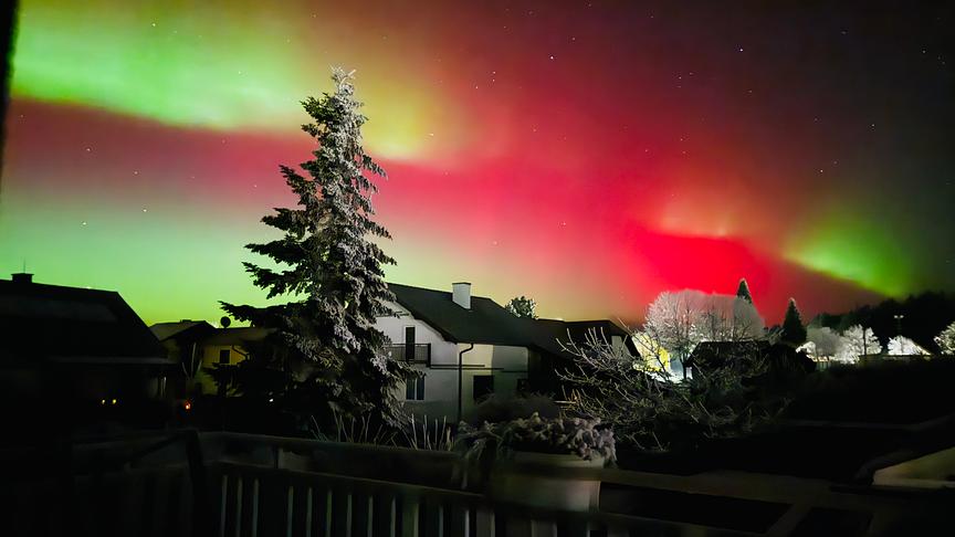 Grüne und rötliche Polarlichter über einem Wohngebiet