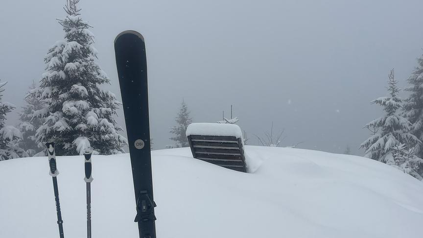 Hohe Schneedecke in der ein Liegestuhl und im Vordergrund Ski und -stöcke zu sehen sind