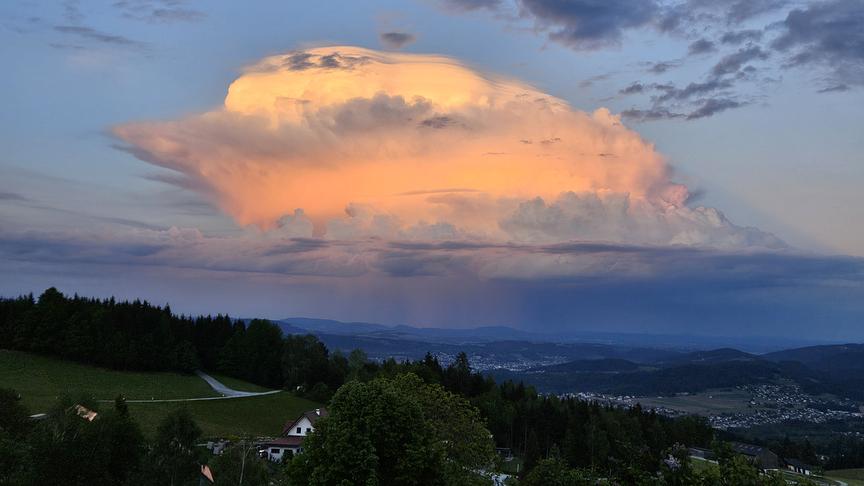 Hohe Wolkenformation in orangem Licht bei ansonsten eher dunklerer Dämmerungsstimmung.
