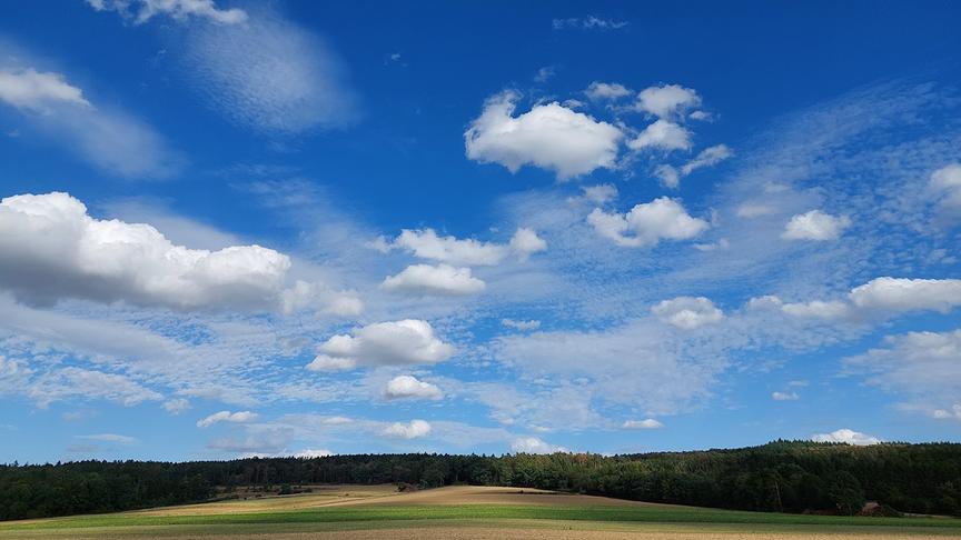 Flache Landschaft mit Wiesen, Feldern und Wald über der interessante wellenartige sowie Schäftchenwolken am Himmel sind.