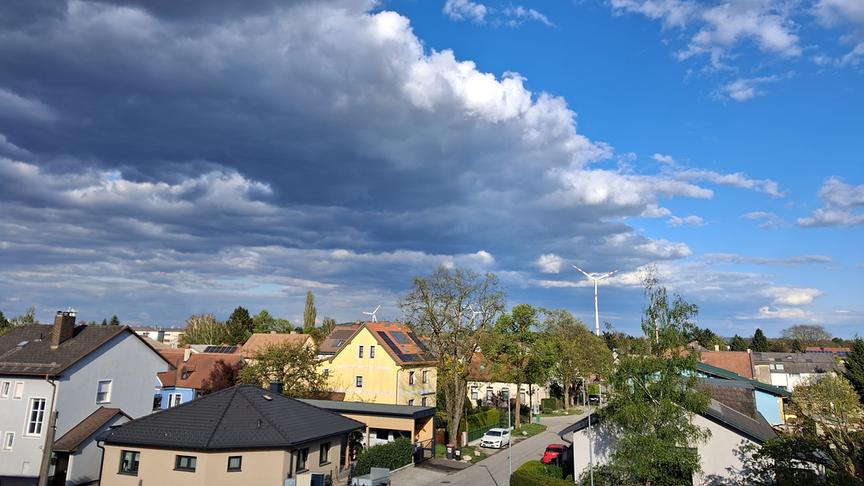 Eine Siedlung über der auf der einen Seite eine dunkle Wolkendecke aufzieht, während auf der anderen Seite noch blauer Himmel ist.