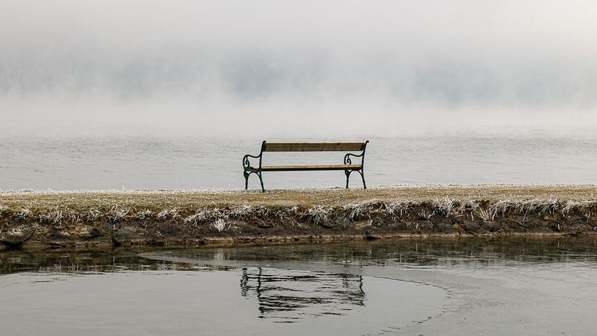 Eine Bank steht auf einem Landsteg mit Blick auf das neblige Gewässer.