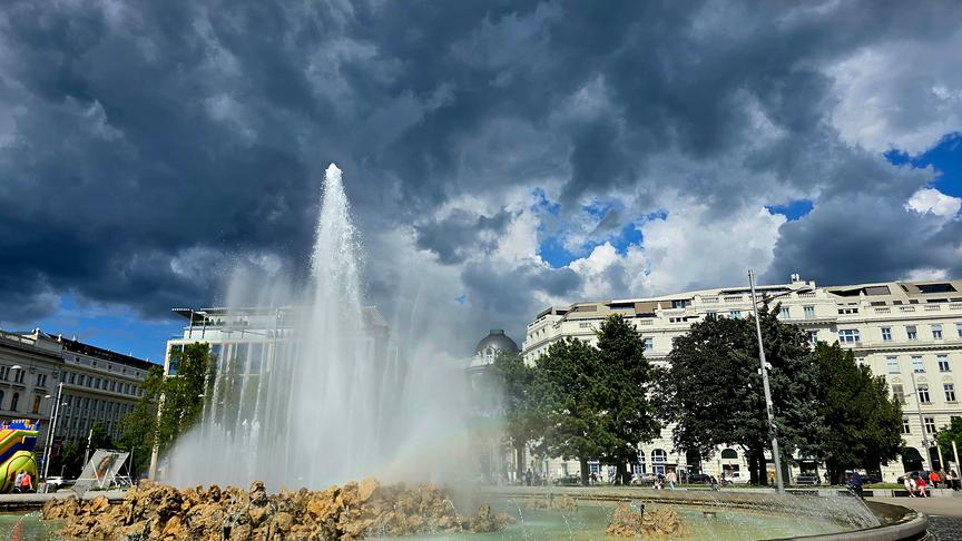 Über einem hohen Springbrunnen ziehen dunkle Wolken auf.