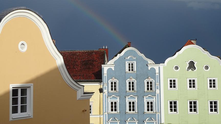 Bunte Häuser bei dunkler Stimmung, ein Regenbogen endet direkt in einem der Hausgiebel.