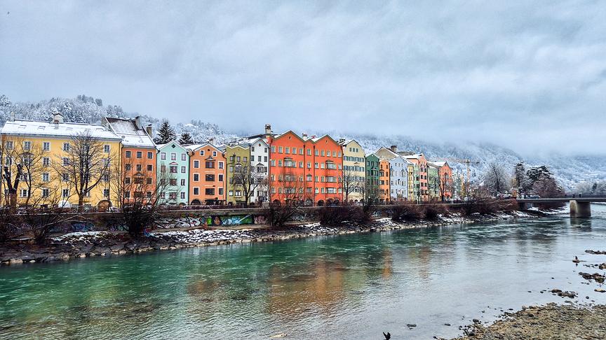 Der Fluss verläuft türkisfarben vor bunten Häusern vorbei, der Himmel ist bedeckt von einer grauen Wolkendecke