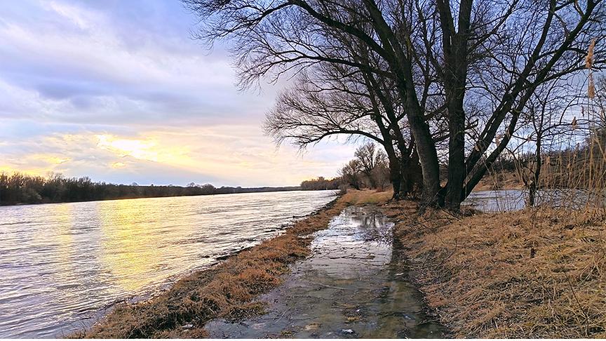 Über die Uferböschung ist der Fluss schon etwas hinausgetreten, im Hintergrund scheint die Sonne schwach durch die Wolken