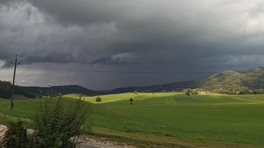 Ein Blick in Richtung Attergau, von Oberwang/Grossenschwandt gesehen. Schwarze Regenwolke ziehen auf. Dazwischen scheint die Sonne durch die Wolken und schafft so eine ganz besondere Atmosphäre.