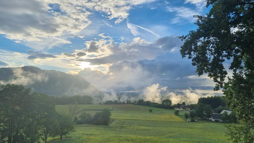Nebel und Wolken über einer grünen, hügeligen Landschaft