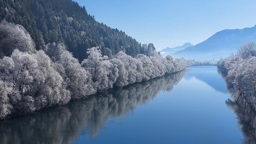 Der Fluss liegt links und rechts umgeben von durch Frost weiß gefärbe Bäume still zwischen den Berghängen.