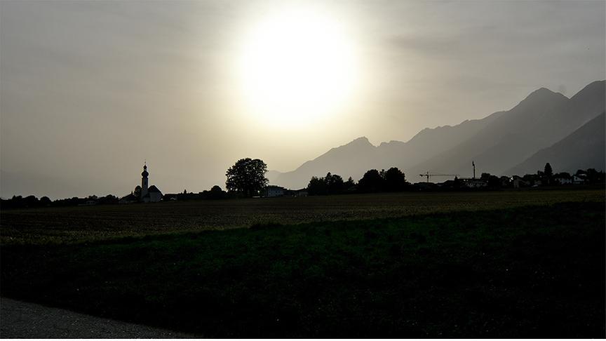 Tiefstehende Sonne über Bergen bei trüber Luft.
