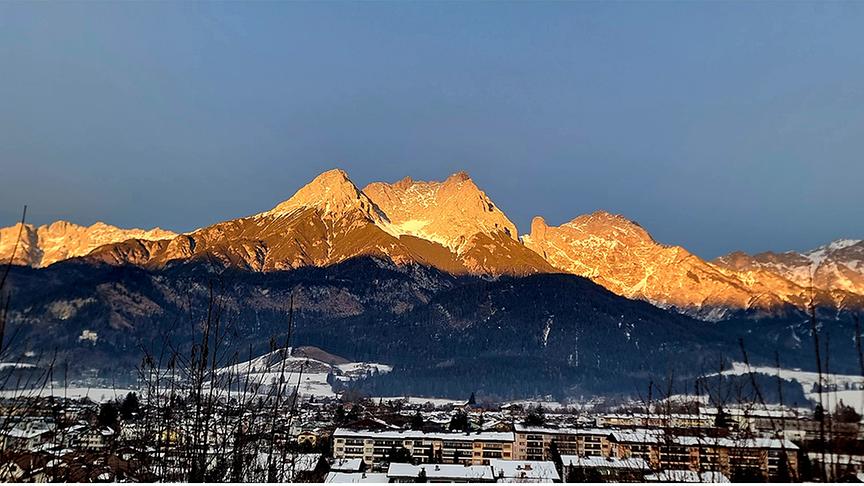 Während die Siedlung im Tal im Schatten liegt, wird der obere Bergkamm von der warm leuchtenden Sonne angestrahlt.