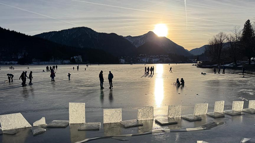 Auf dem zugefrorenen See bewegen sich mehrere Leute im Sonnenuntergangslicht.