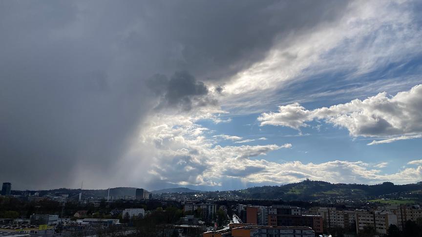 Links: Graue Wolken ziehen sich bis zum Boden hinab, rechts: blauer Himmel mit einigen, wenigen Wolken
