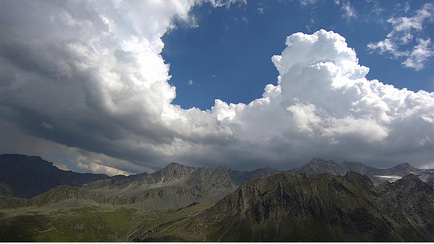 Bergpanorama mit hohen, dichten Wolkenformationen am Himmel. 