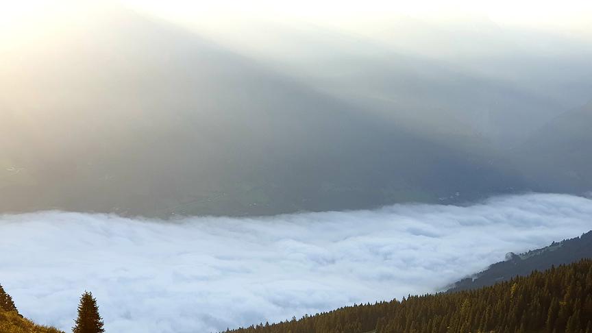 Von einem Berg hinab fotografiertes Tal, das bedeckt mit einer dichten Nebelschicht ist.
