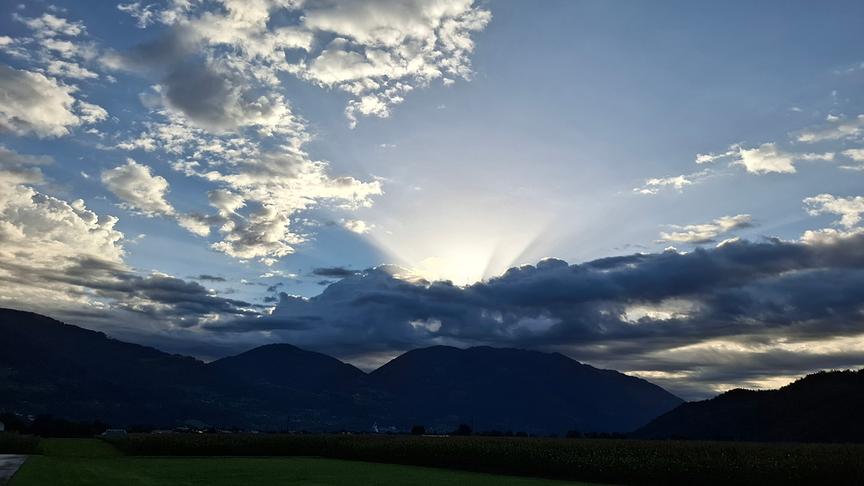 Sonne scheint über Bergen hinter Wolken hervor.