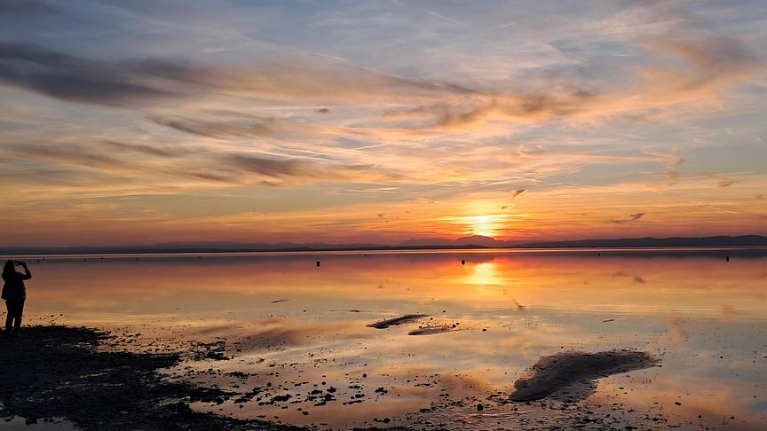 Stimmungsvoller Sonnenuntergang über einem ruhigen See mit orangefarbenem Himmel und Spiegelungen im Wasser.